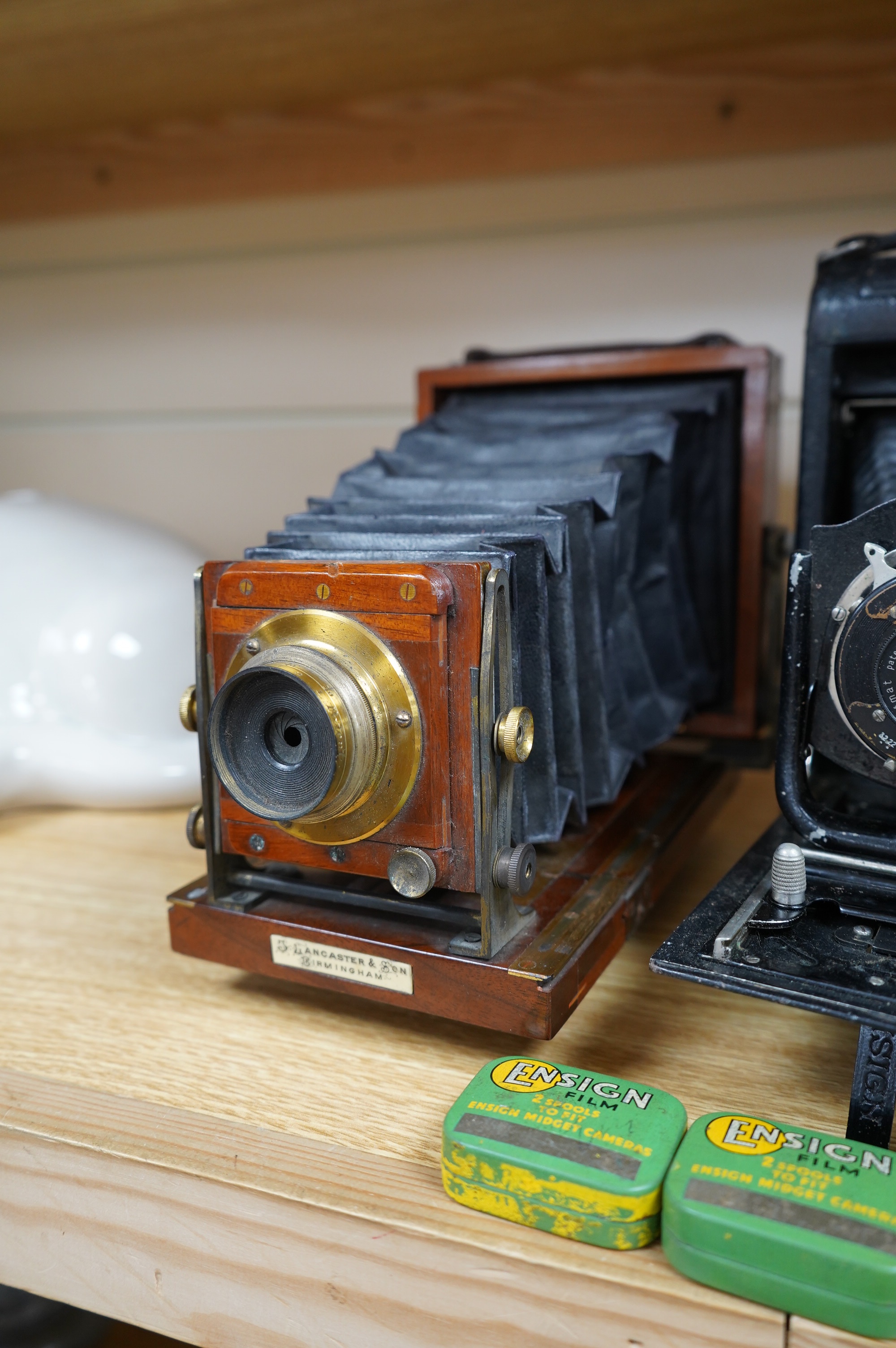 Two cameras; one late 19th century by Lancaster & Son, together with an Ensign bellows camera with two tins of spools of film. Condition - fair to good